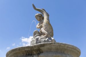 Detail putta na delfínu na vrcholku kašny